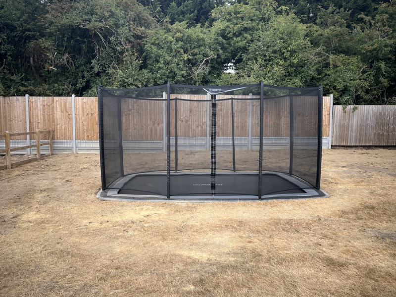 Sunken rectangular trampoline with safety net installed flush with the lawn in an Essex garden